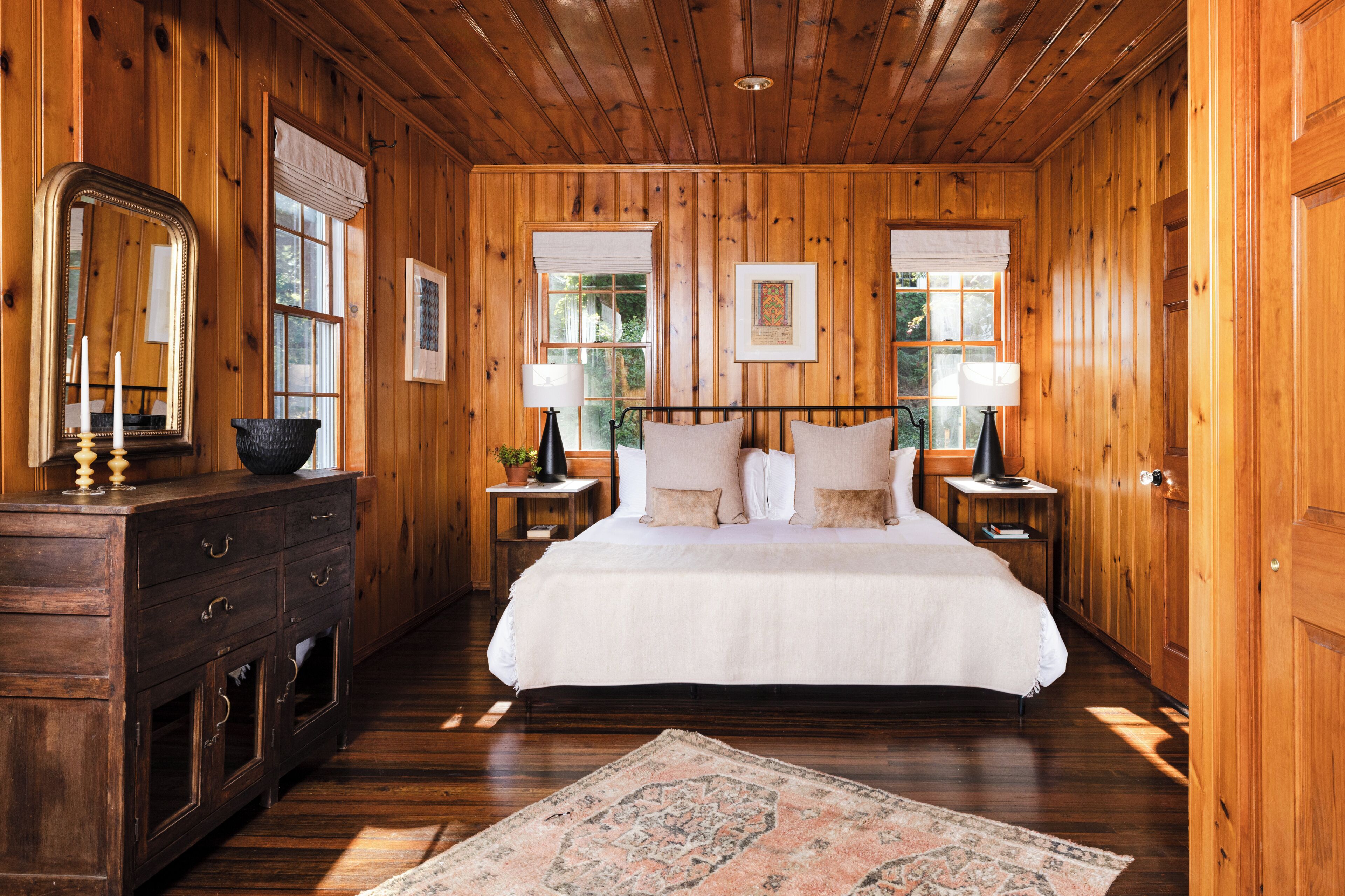 A wooden-paneled bedroom with a bed, nightstands, a dresser, and a mirror.