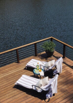 Une terrasse avec des chaises longues et une table, donnant sur une étendue d’eau.