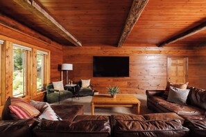 Ein gemütliches Blockhaus-Interieur mit Holzwänden, Ledersofas, einem Couchtisch und einem Fernseher.