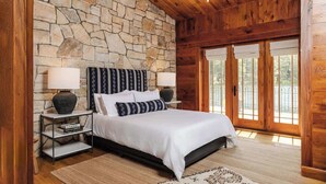 A bedroom with a stone wall, wooden ceiling, and a large bed with white bedding. - Private 37 Acre Lake Estate on 164 Acres - 11 BR (Highland)