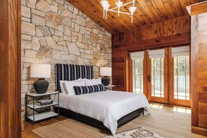 Ein Schlafzimmer mit Steinsturz, Holzbalkendecke und einem großen Bett mit weißer Bettwäsche.