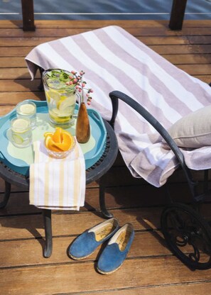 Ein Tisch mit einer Limonadenkanne, Gläsern und einer Serviette auf einem blauen Tablett, ein Paar blaue Schuhe und ein gestreiftes Handtuch auf einem Stuhl.