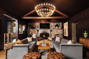 Ein gemütliches Wohnzimmer mit Kamin aus Stein, Ledersofas und Holzbalkendecke.