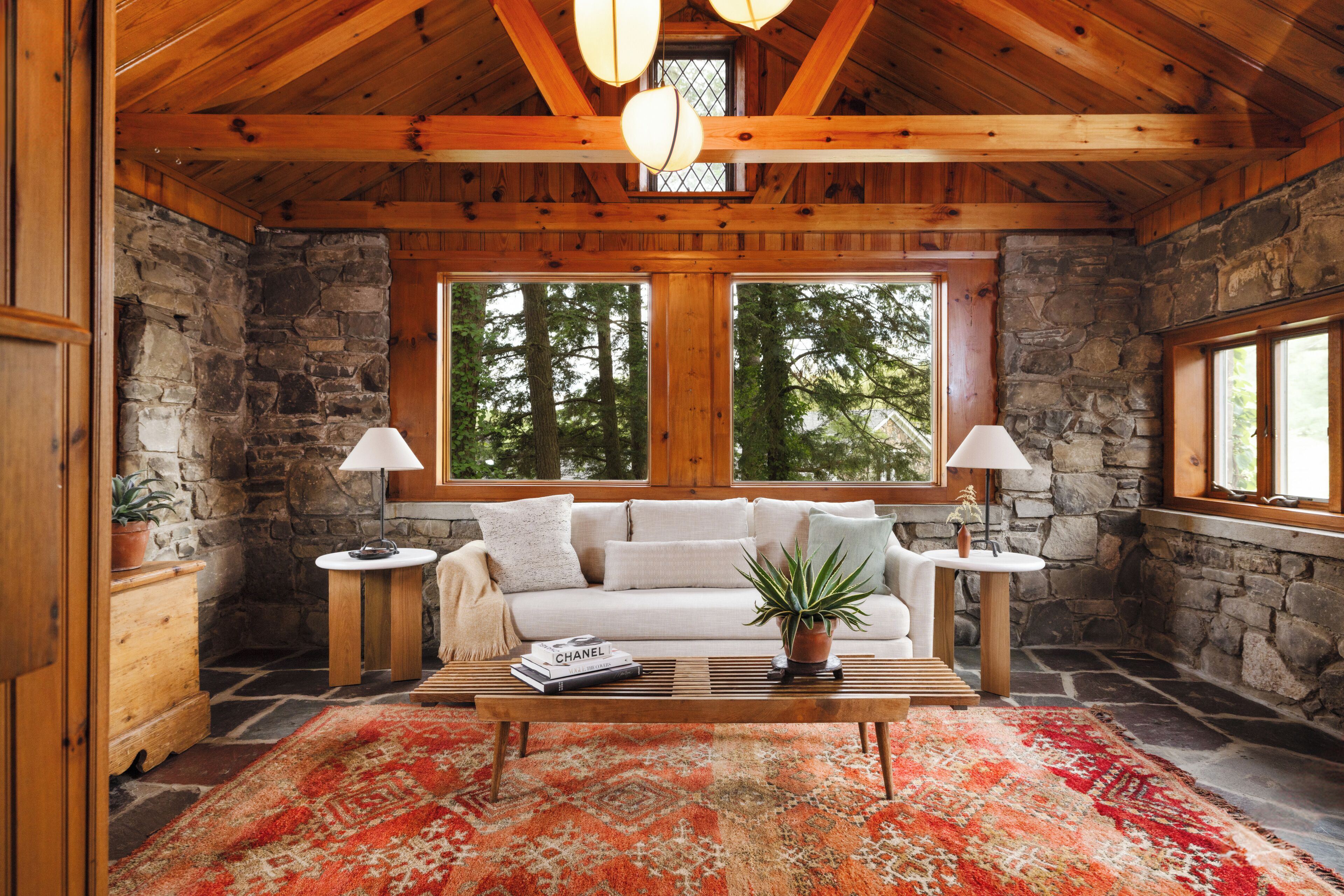 A cozy interior with a stone wall, wooden ceiling, a sofa, a coffee table, and two lamps.
