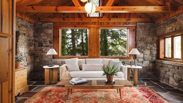 A cozy interior with a stone wall, wooden ceiling, a sofa, a coffee table, and two lamps.