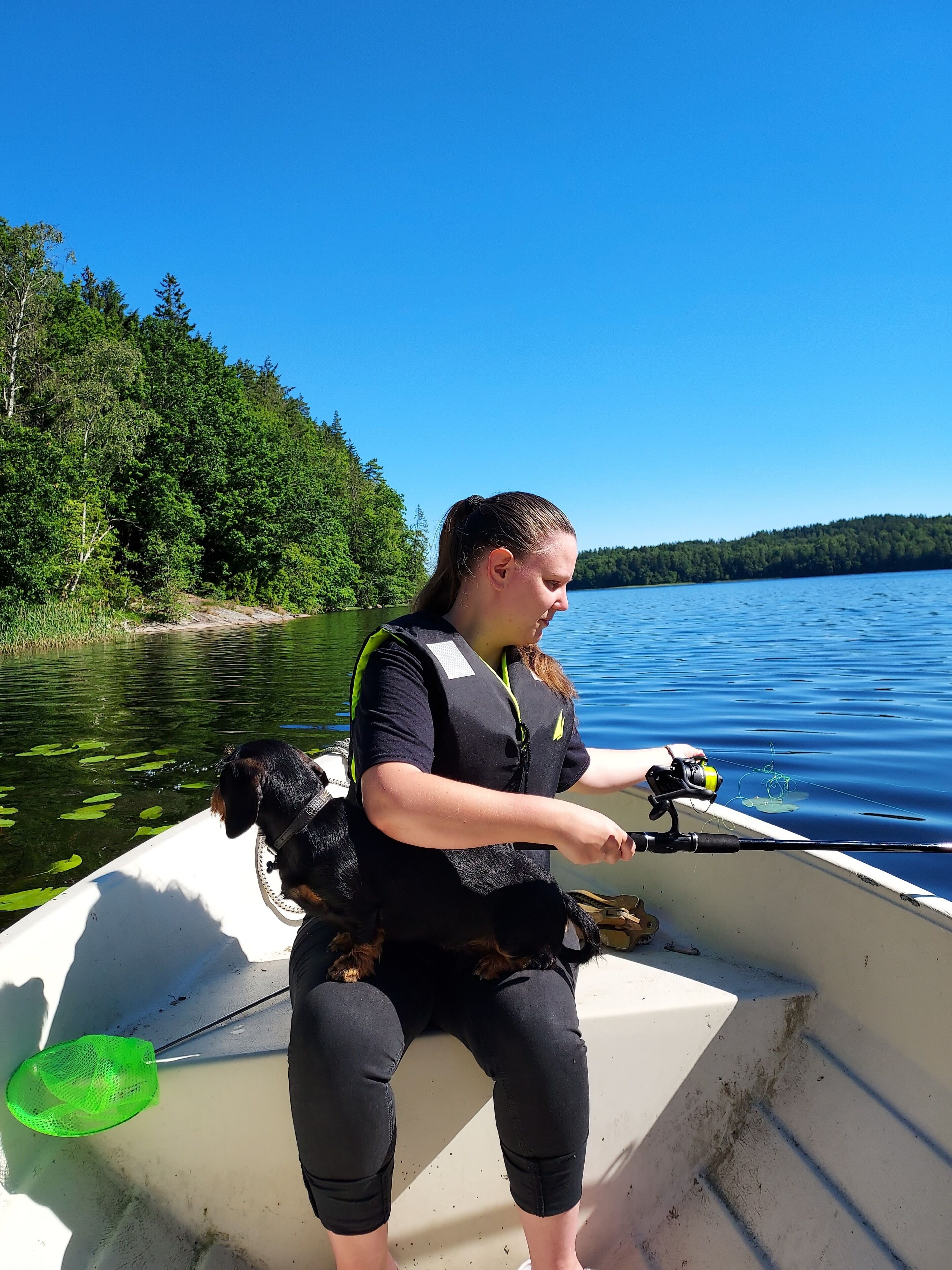 Une personne pêchant depuis un bateau sur un lac dont les rives sont bordées d’une forêt.
