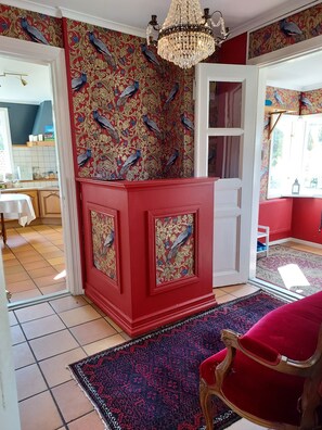 A room with a red accent wall, a peacock-themed wallpaper, a chandelier, and a red velvet chair. - älgbergets b&b (Ucklum)