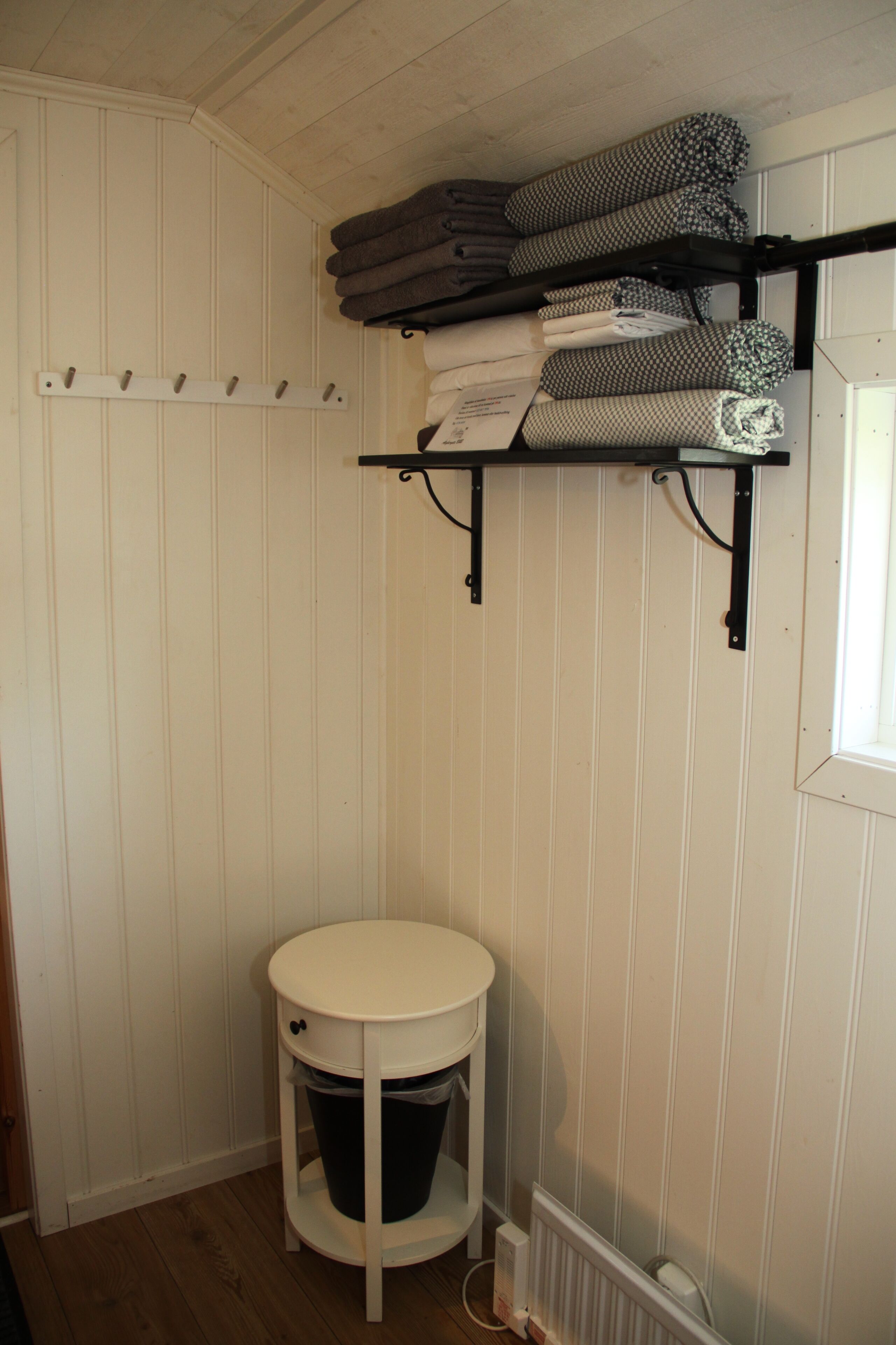 A small bathroom with a white sink, a white toilet, a white trash bin, and a shelf with folded towels.