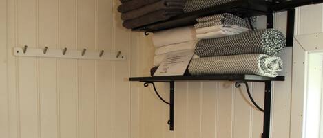 A small bathroom with a white sink, a white toilet, a white trash bin, and a shelf with folded towels.