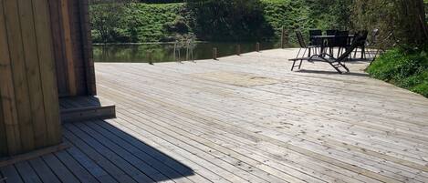 Un pontile di legno con vista su un lago e alberi, un edificio in legno e un tavolo con sedie.