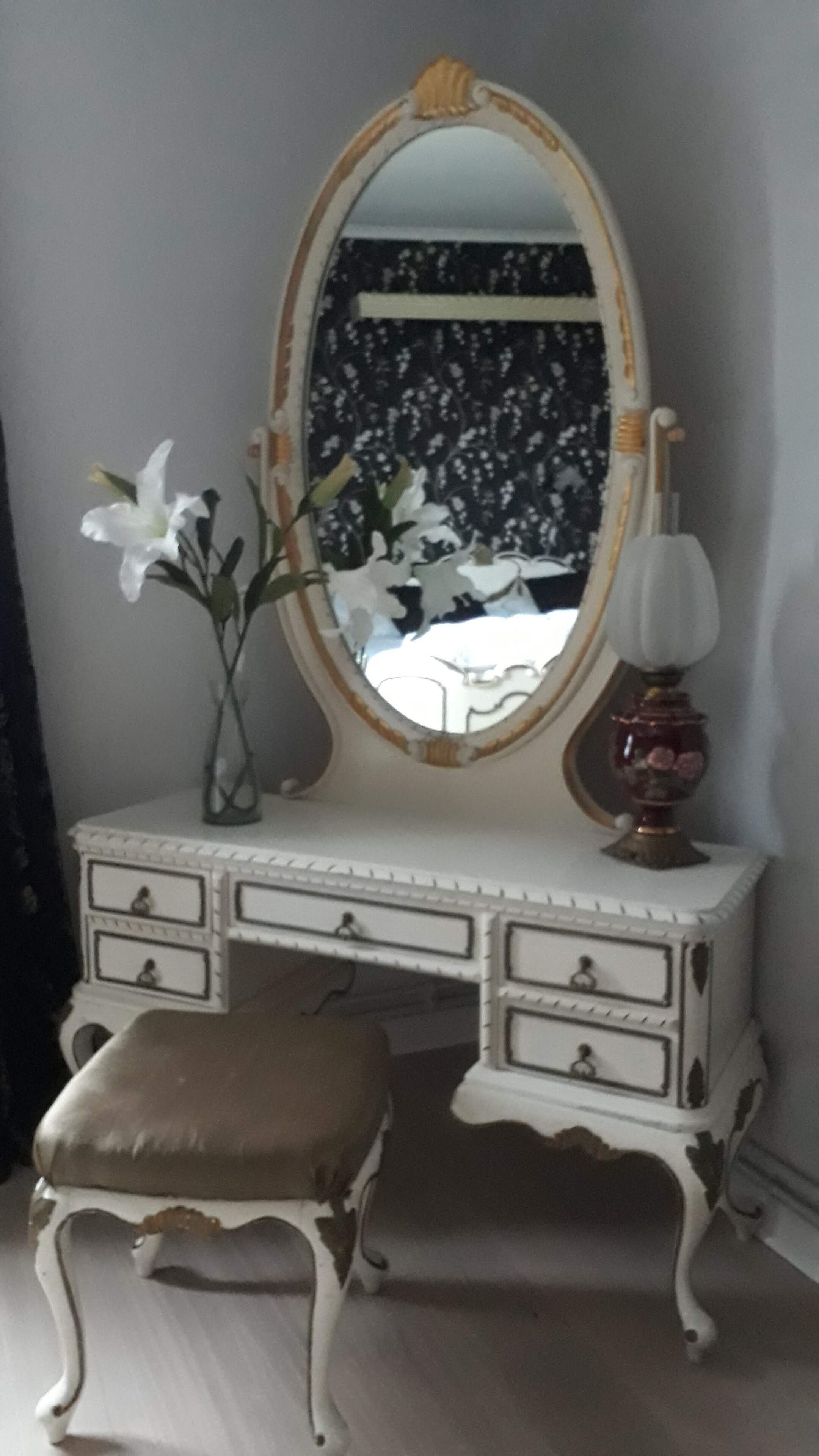 A white vanity with a mirror, a lamp, and a vase with flowers.