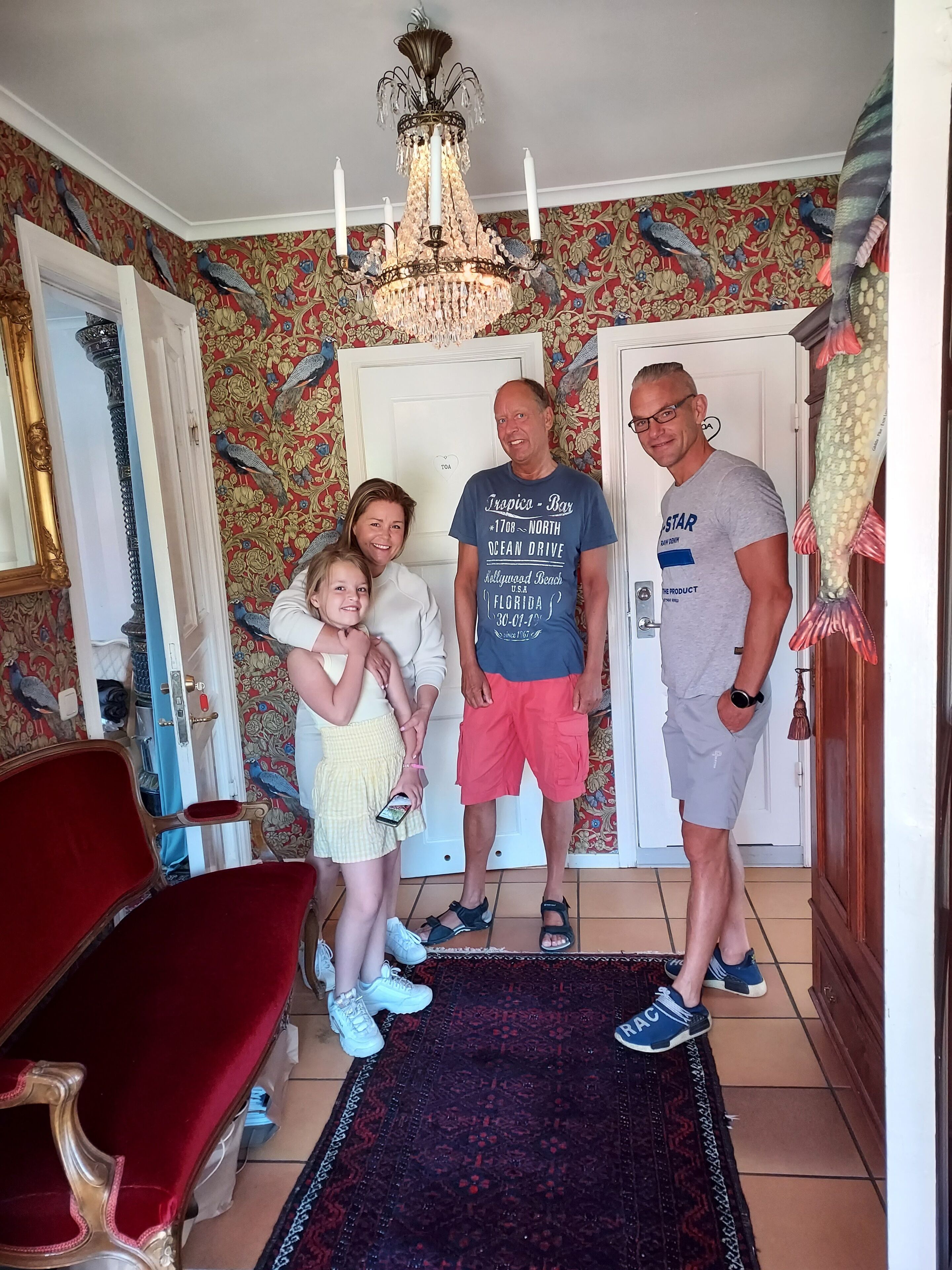 A room with a chandelier, patterned wallpaper, a red chair, and a door with a fish decoration.