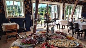 A buffet table with various food items, a decorative candle centerpiece, and a view of the outdoors through large windows. - älgbergets b&b (Ucklum)
