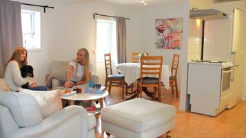 Sala de estar con sofá, mesa de comedor y sillas, zona de cocina con refrigerador y estufa, y ventana con cortinas.