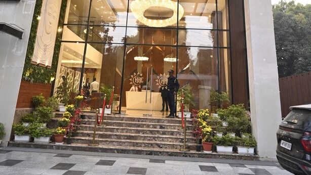 Una entrada de hotel moderna con fachada de vidrio, un mostrador de recepción de madera y una escalera que conduce al vestíbulo.
