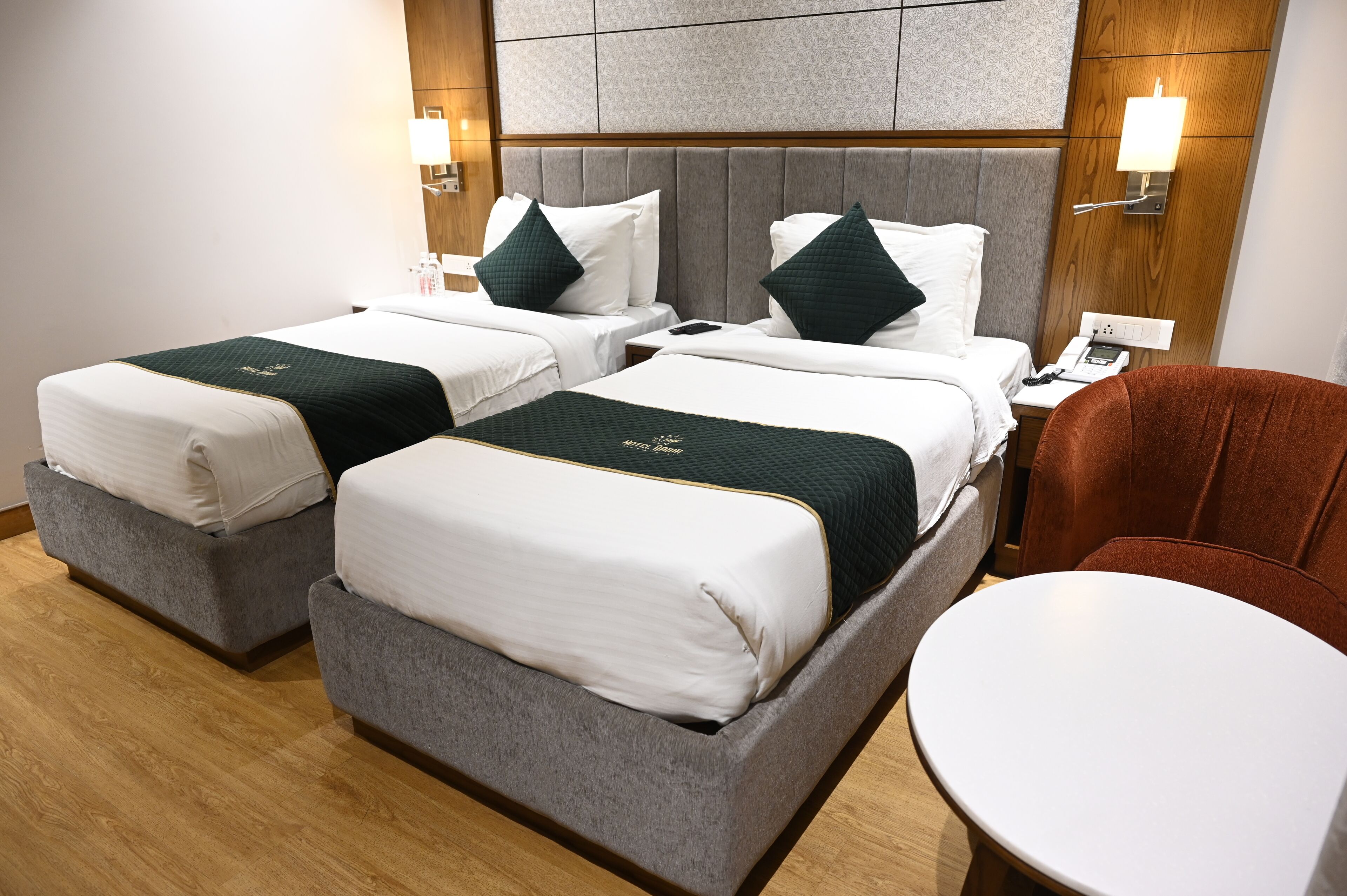 A hotel room with two beds, a round table, and a wooden floor.