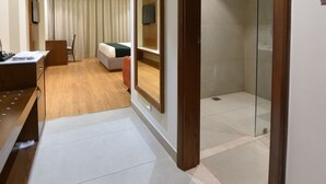 Habitación de hotel con escritorio, silla, cama y zona de ducha.