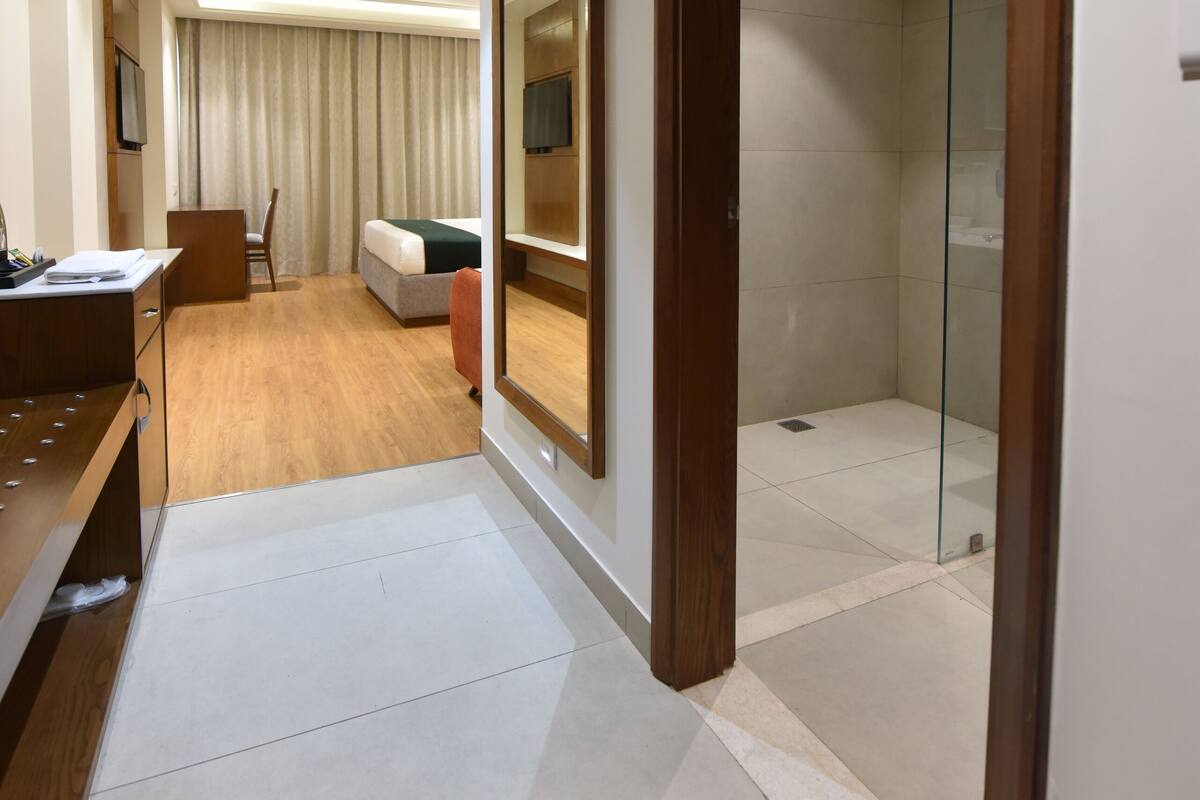 A hotel room with a desk, chair, bed, and a shower area.