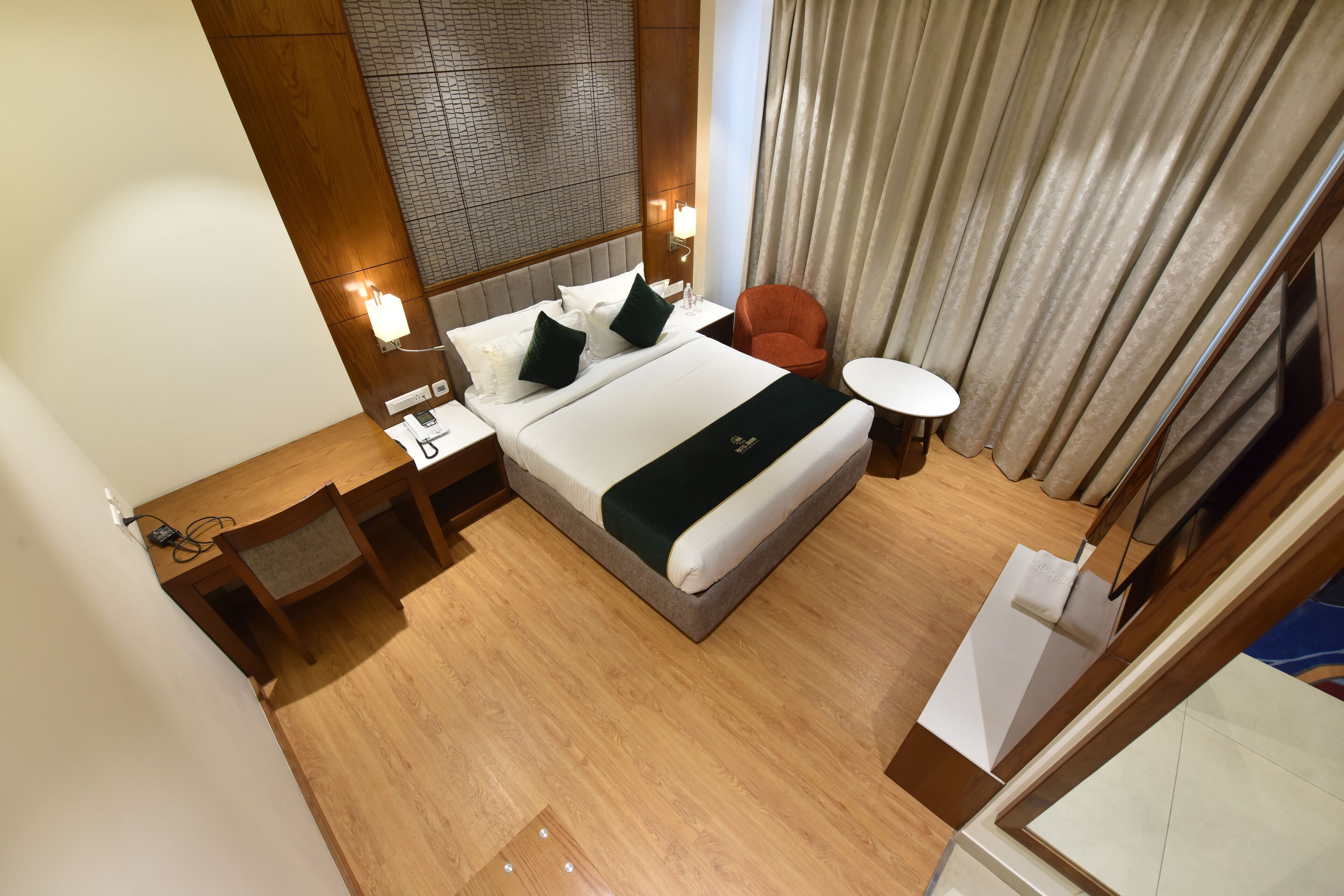 Una habitación de hotel con una cama grande, cabecera de madera, mesita de noche, sillón rojo y una pequeña mesa redonda.