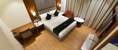 Una habitación de hotel con una cama grande, cabecera de madera, mesita de noche, sillón rojo y una pequeña mesa redonda.