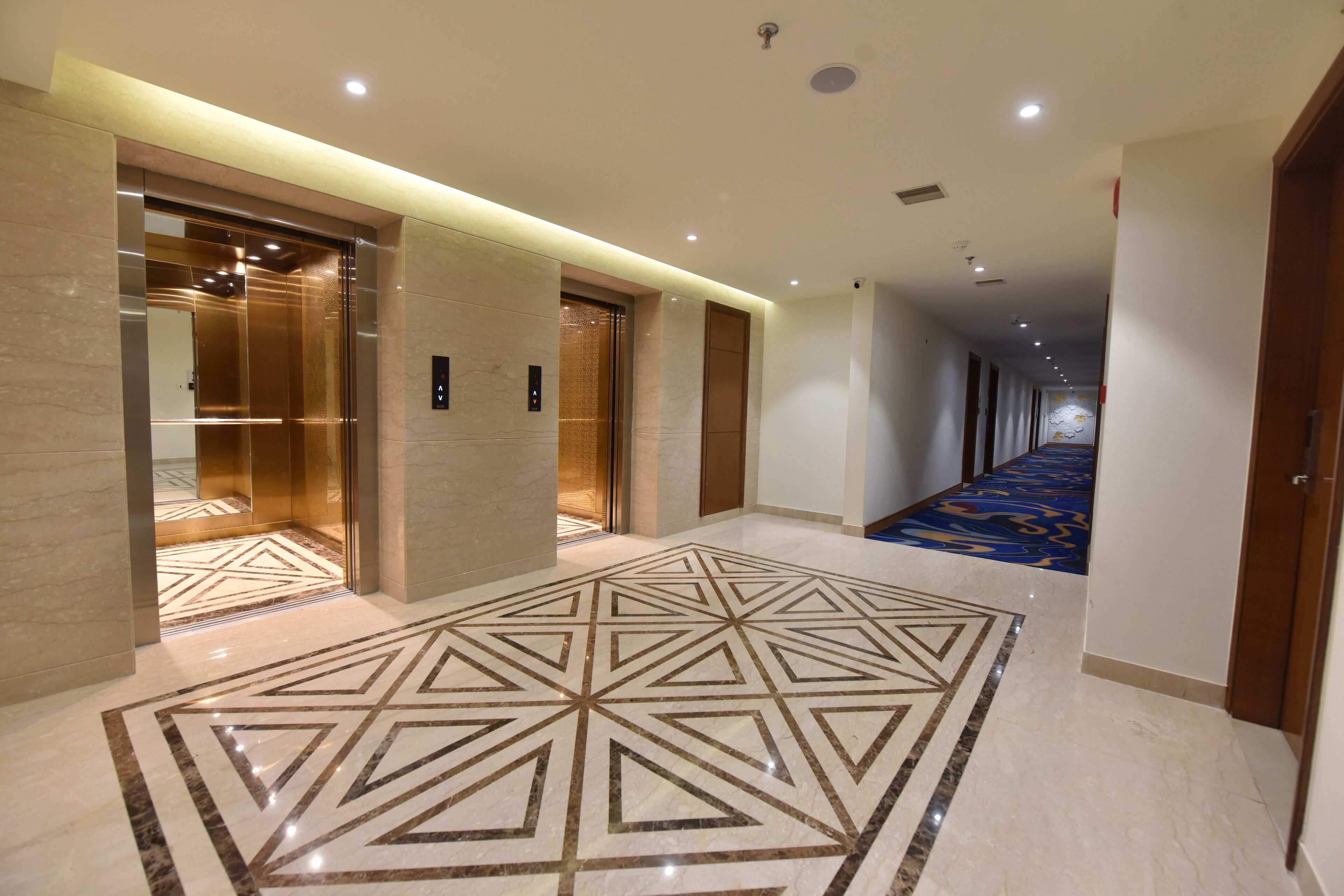 Pasillo de hotel con ascensores, piso estampado y área alfombrada.