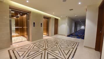 A hotel corridor with elevators, a patterned floor, and a carpeted area.