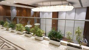Un vestíbulo moderno con piso de mármol, plantas en macetas, una lámpara de cristal grande y barandilla de vidrio.