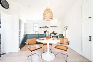 Una cocina moderna con armarios blancos, una mesa redonda de comedor con cuatro sillas de mimbre y una lámpara colgante de ratán.