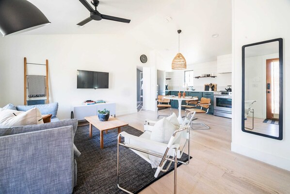 A modern living room with a sofa, coffee table, and a TV. There is a kitchen area with a dining table and chairs.