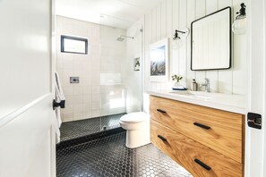 Un baño moderno con ducha, inodoro y tocador con espejo y lavabo.