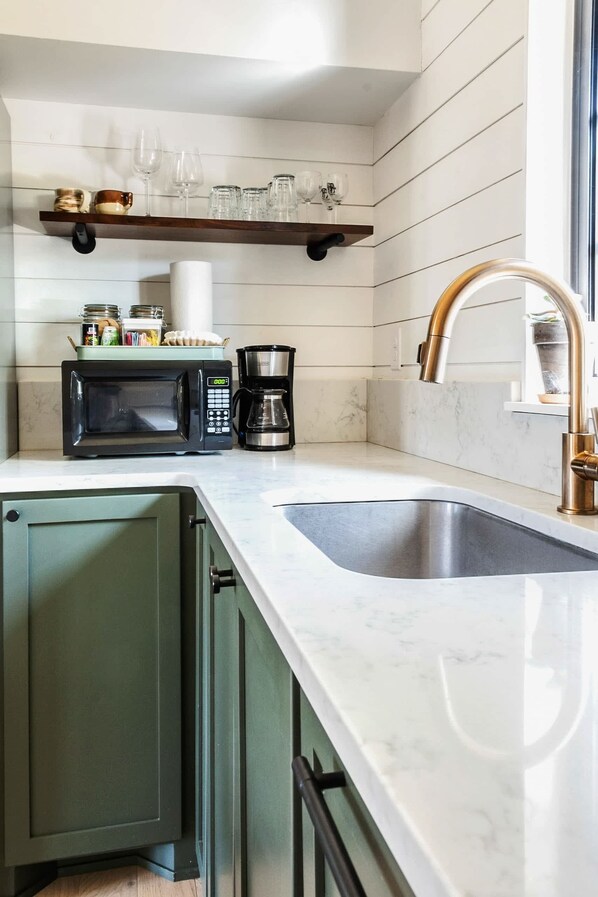 A kitchen with a built-in microwave, coffee maker, and a stainless steel sink.