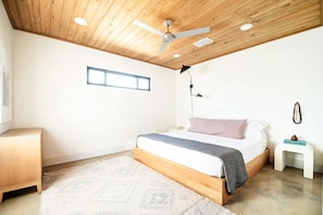 A bedroom with a wooden ceiling, a bed with a grey blanket, a bedside table, and a nightstand.