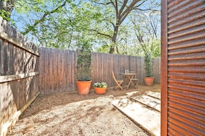 A backyard with a wooden fence, two potted plants, a folding table, and a chair.