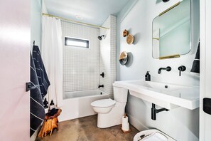 Un baño con bañera, inodoro, lavamanos y espejo.