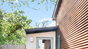 Ein kleines, modernes Haus mit Holzzaun, einem Betonweg, der zur Tür führt, und einem Blumentopf.