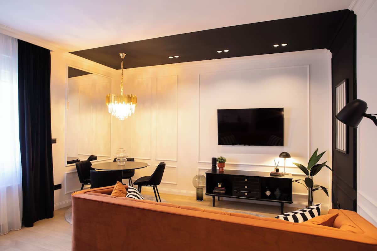 Un salon moderne comprenant un canapé, une table à manger, un lustre, un téléviseur et une plante.