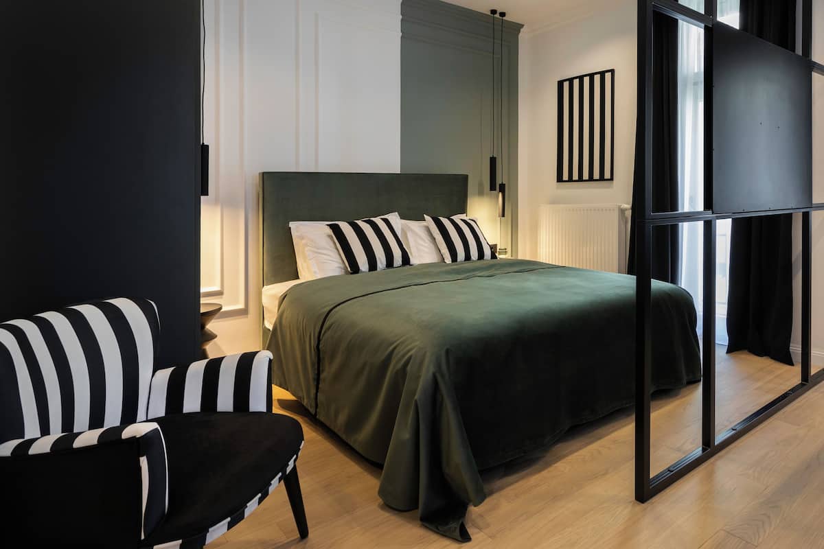 Une chambre à coucher moderne, dotée d’un grand lit, d’un canapé à rayures noires et blanches et offrant une vue à travers une cloison en verre.