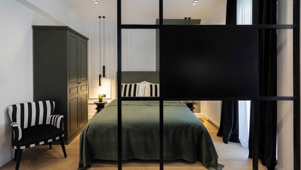 Ein modernes Schlafzimmer mit einem großen Bett, einem dunkelgrünen Polsterstuhl und einem Kleiderschrank.