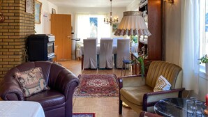 Een woonkamer met een open haard, leren fauteuils, een salontafel en een eethoek op de achtergrond.