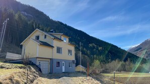 Een tweelaags huis met garage, omgeven door een glooiend landschap en een heldere lucht.