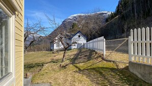 Een landelijk gelegen pand met een wit huis, een omheinde tuin en een berg op de achtergrond.