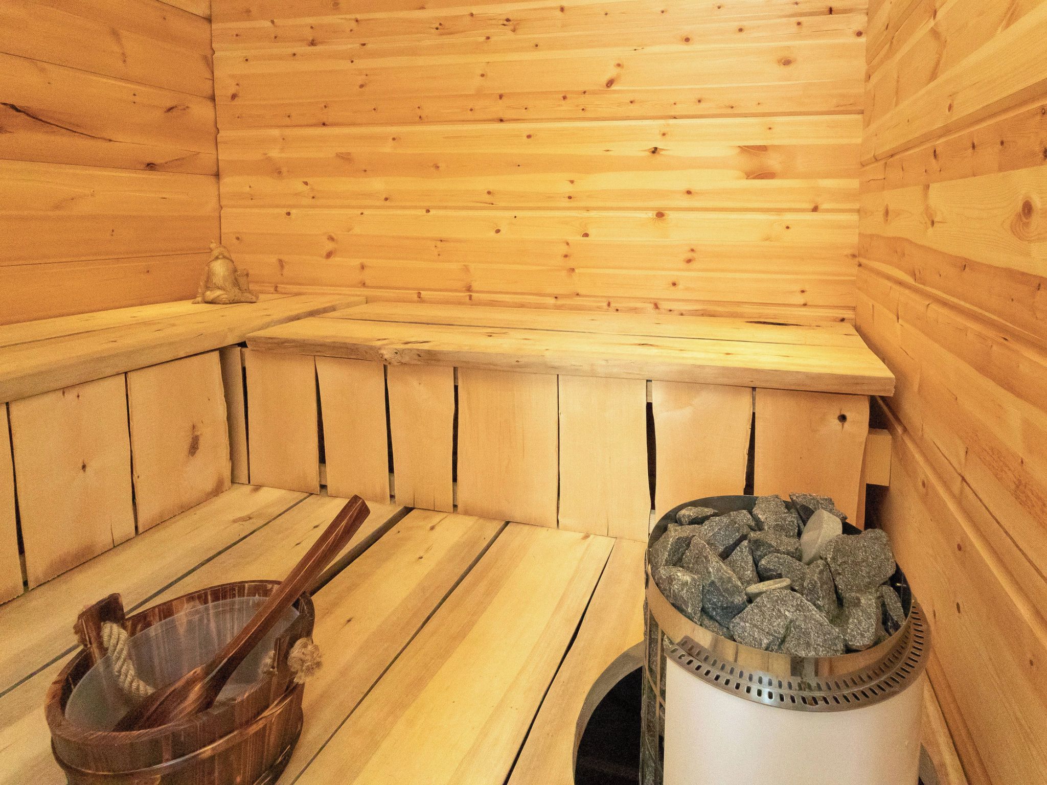 Un sauna con paredes y bancos de madera, un balde de madera y un cubo de basura.