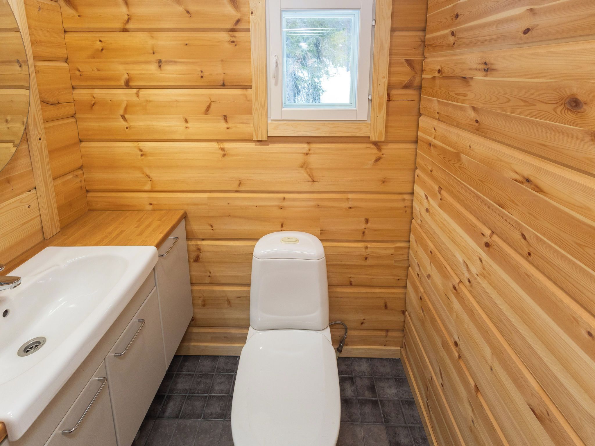 A small, compact bathroom with wooden walls, a white toilet, and a bathtub.