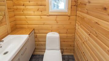 A small, compact bathroom with wooden walls, a white toilet, and a bathtub.