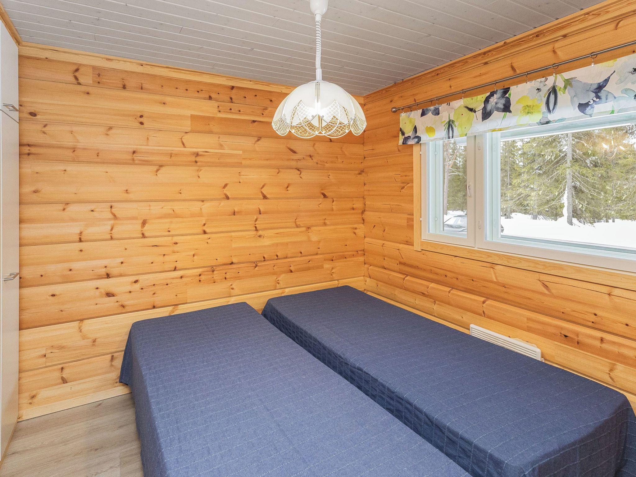Quarto de cabana com paredes de madeira, janela com vista para árvores e cama com colchão azul.