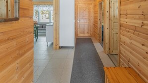 Een houten blokhut van binnen met een centrale gang, een eethoek met tafel en stoelen, en een koelkast.