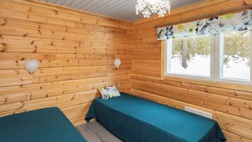 A cabin with two beds, wooden walls, a window with a floral curtain, and a chandelier.