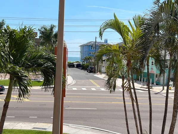 Une vue de rue avec des palmiers, un immeuble bleu et des voitures garées.