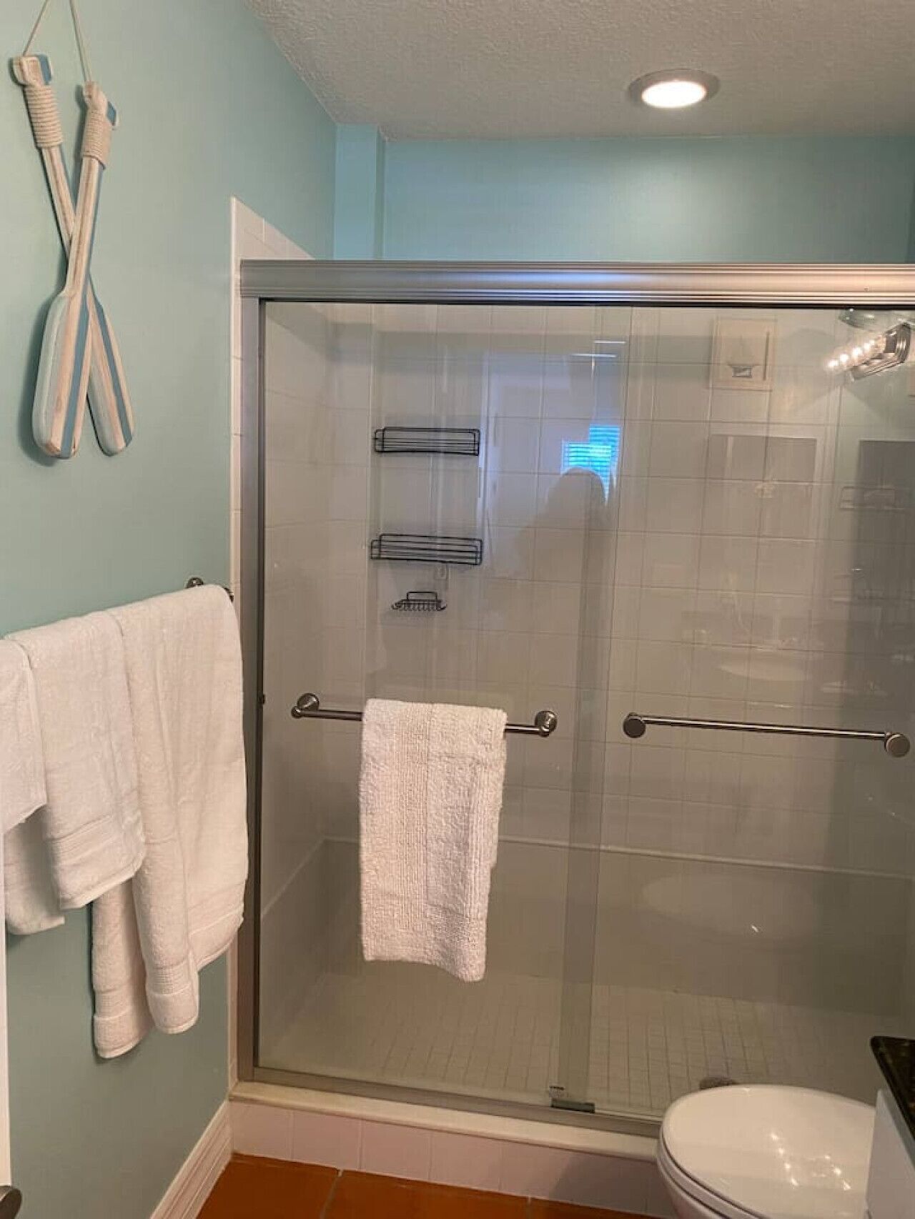 Eine Duschkabine mit Glas, ein weißes Handtuch auf einem Ablagekorb, eine Toilette und ein Handtuchhalter mit Handtüchern.