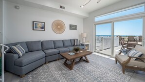 A living room with a gray sectional sofa, a wooden coffee table, and a view of the ocean through large sliding glass doors. - Beautiful, modern, 4 bedroom oceanfront townhome! (Ocean City)